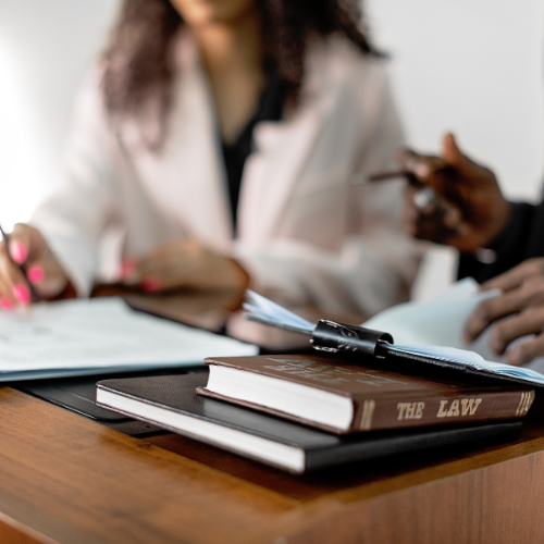 Two professionals reviewing legal documents at a desk with law books in the foreground.