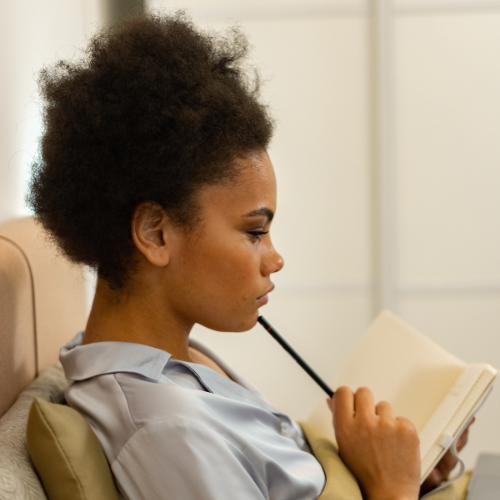 young black woman sitting on couch with a journal and a pencil